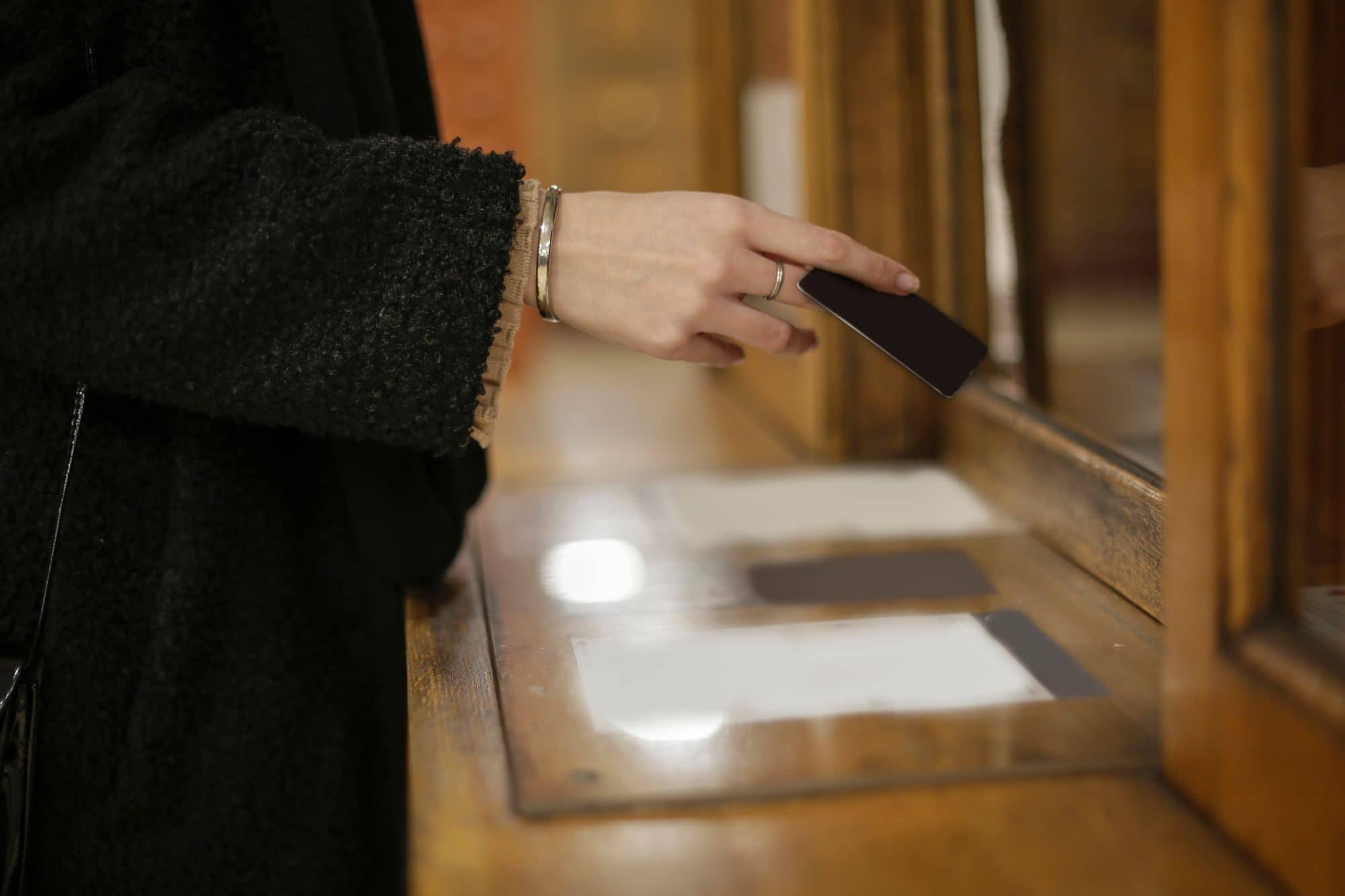A customer slides a card across a wooden bank counter window