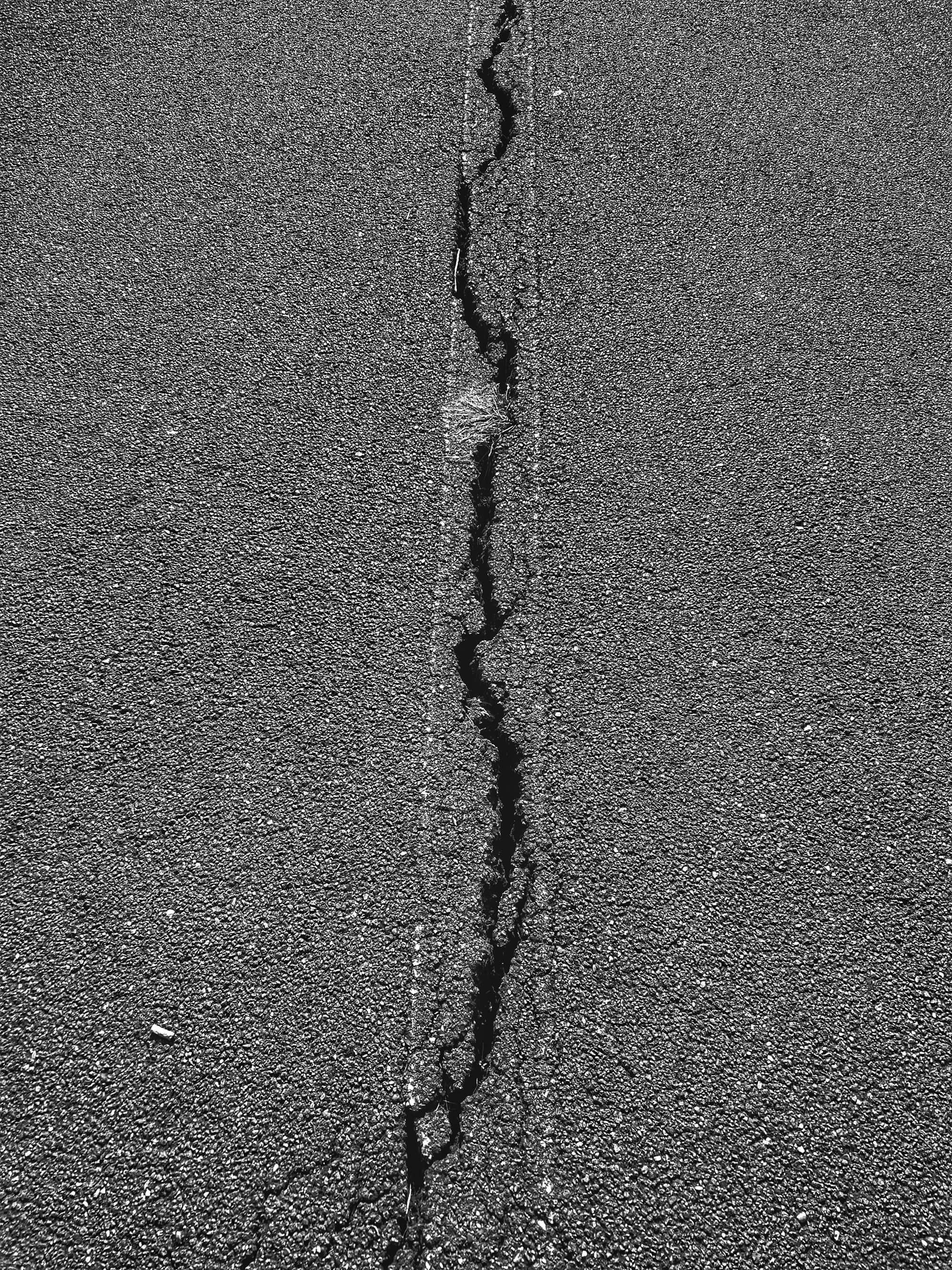 An open, unsealed crack running through gray asphalt