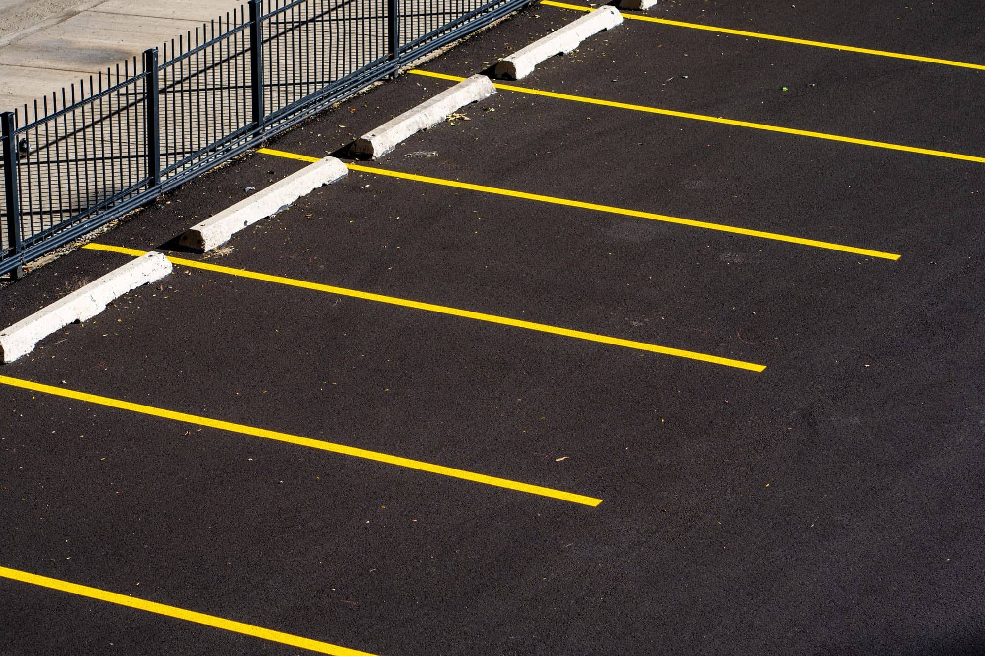 Fresh yellow parking stall lines and concrete wheel stops on a newly sealed lot