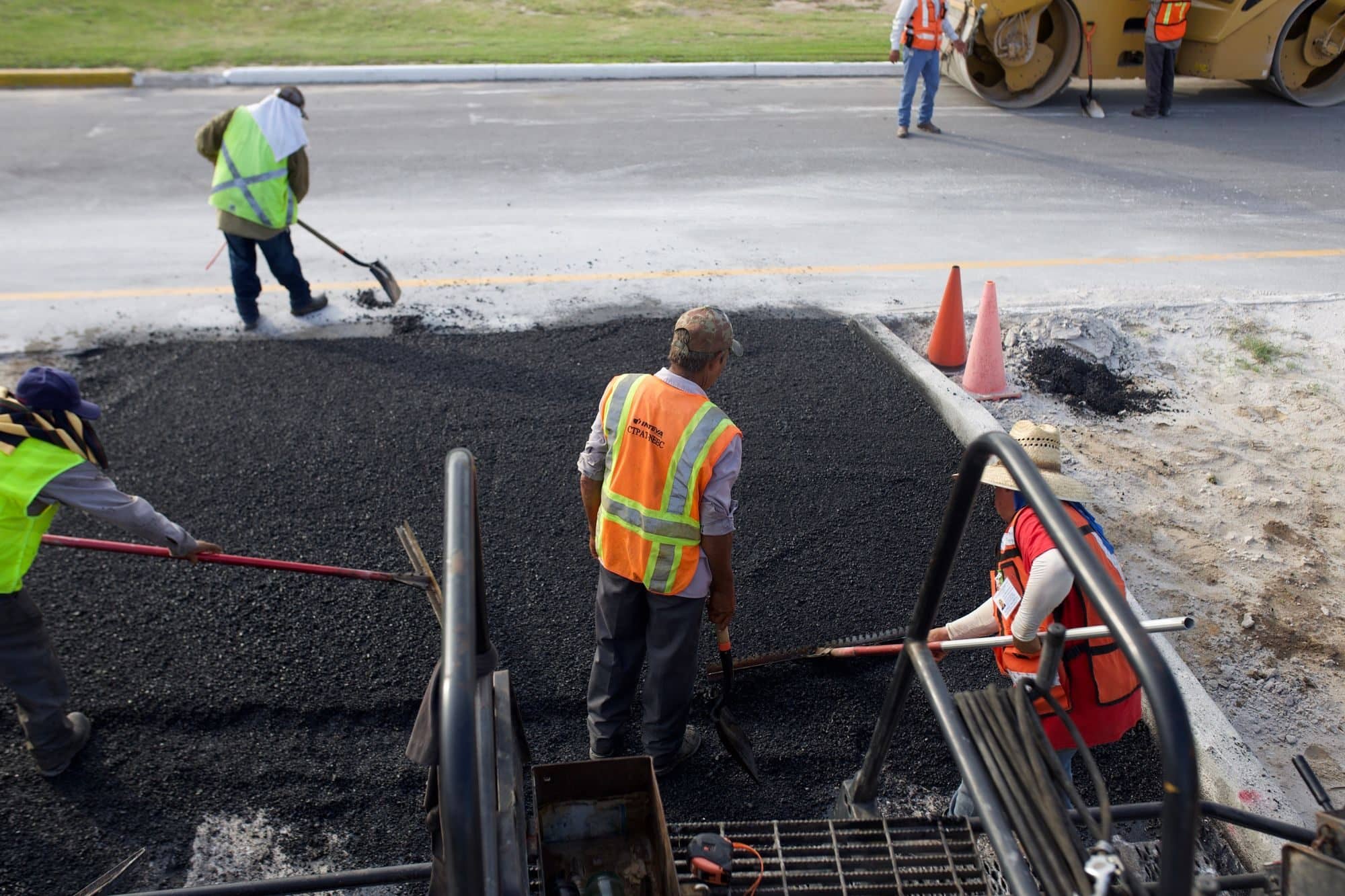 A crew in safety vests shovels and rakes hot asphalt into a pavement patch