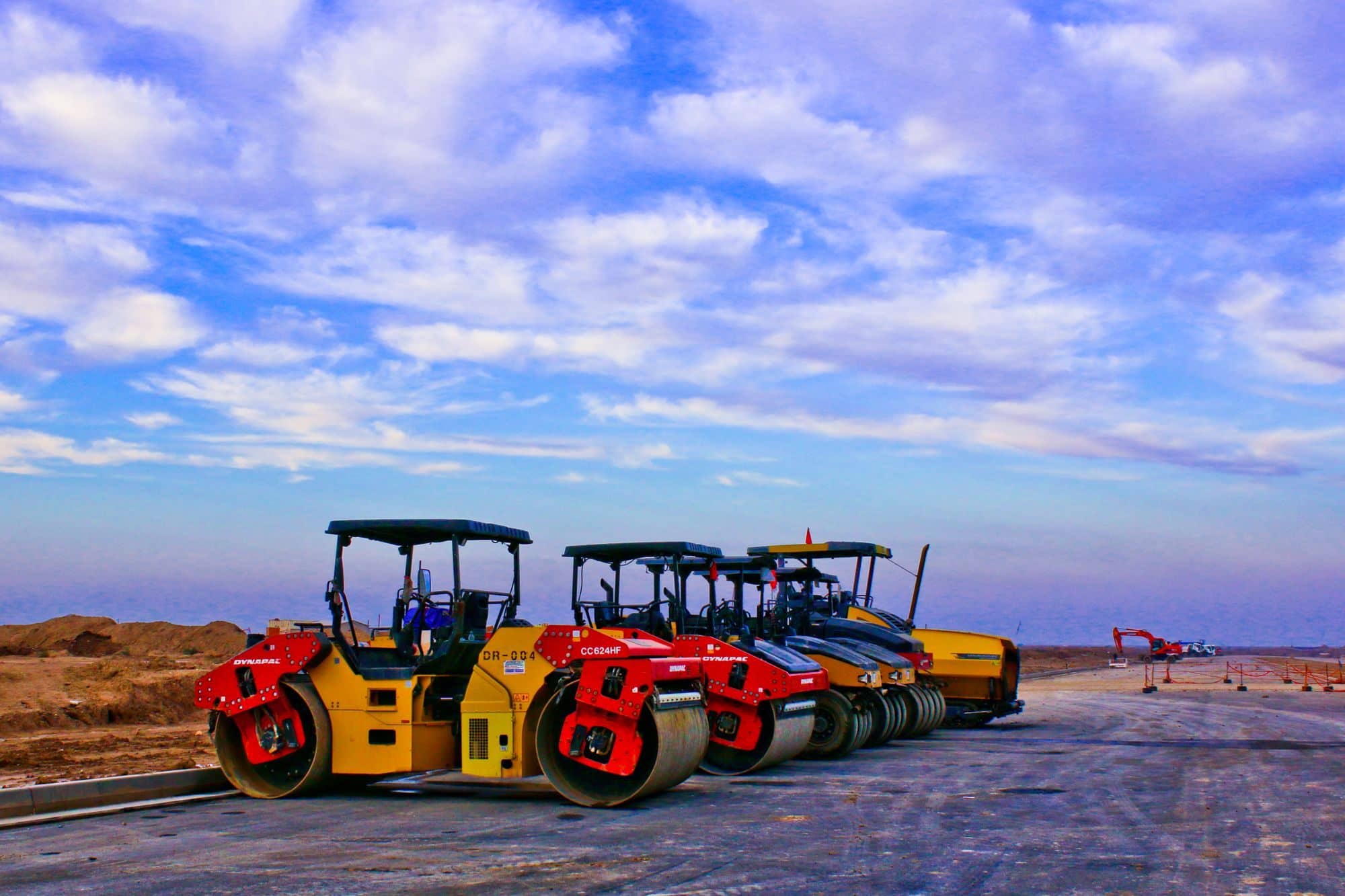 Three double-drum asphalt rollers parked in a row on a paving site