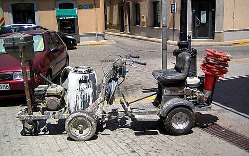 A walk-behind line striping machine with a paint tank, parked at a street corner