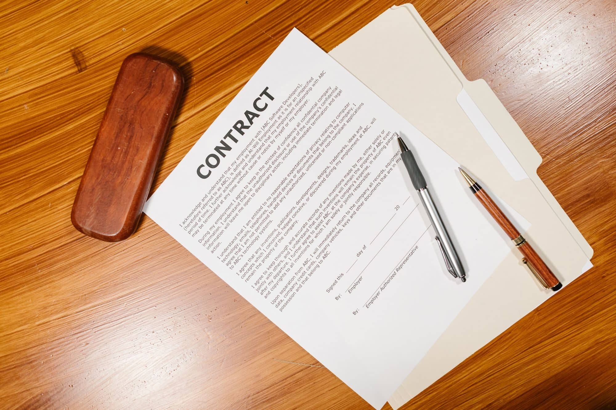 A printed contract on a file folder with two pens on a wooden desk