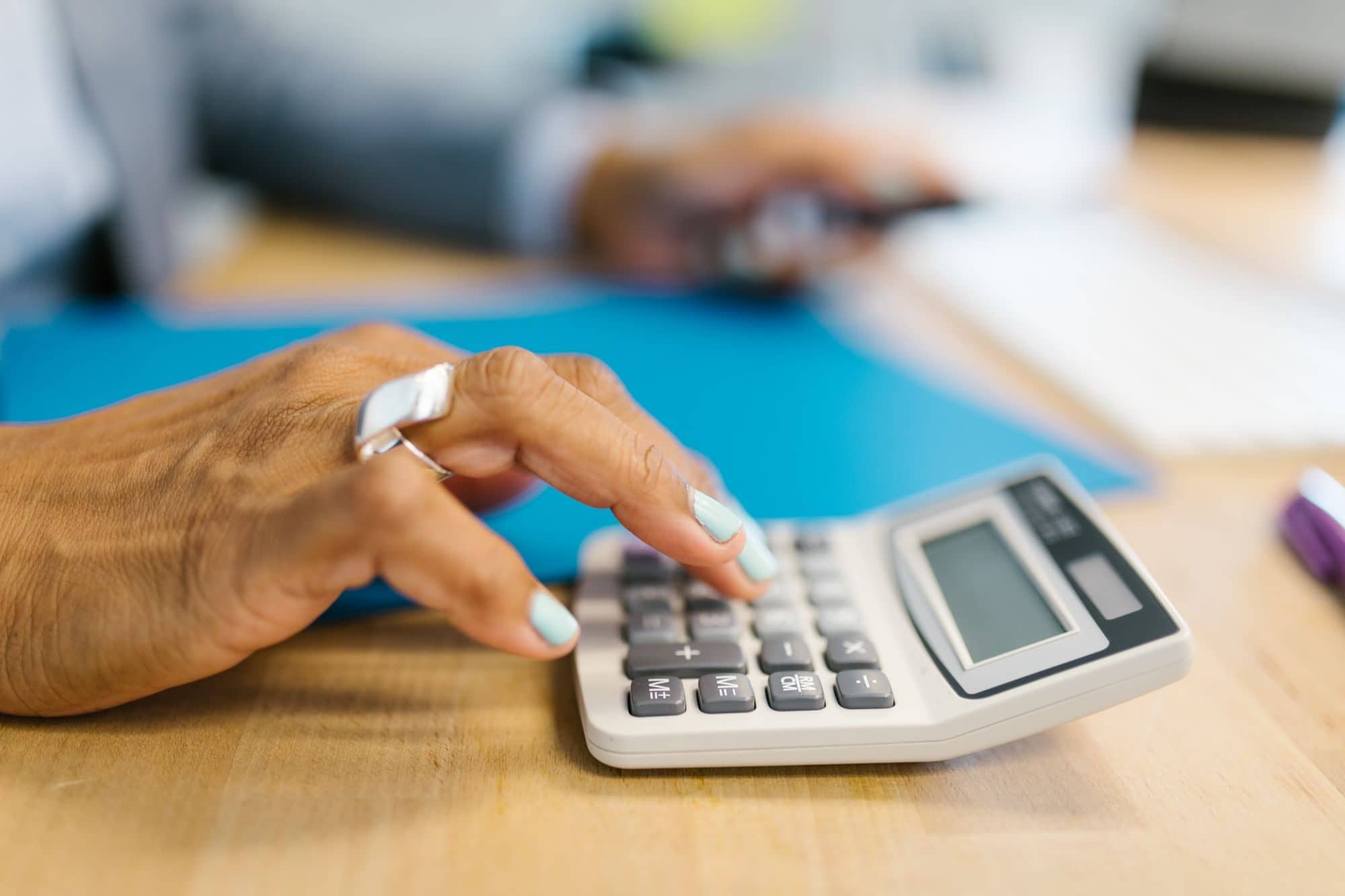 A hand enters numbers on a white desk calculator