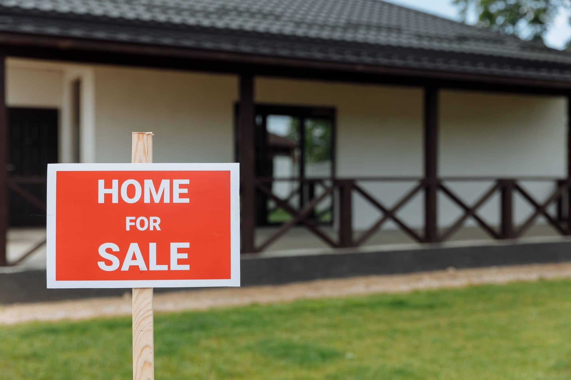 A red Home for Sale sign on the lawn in front of a single-story house