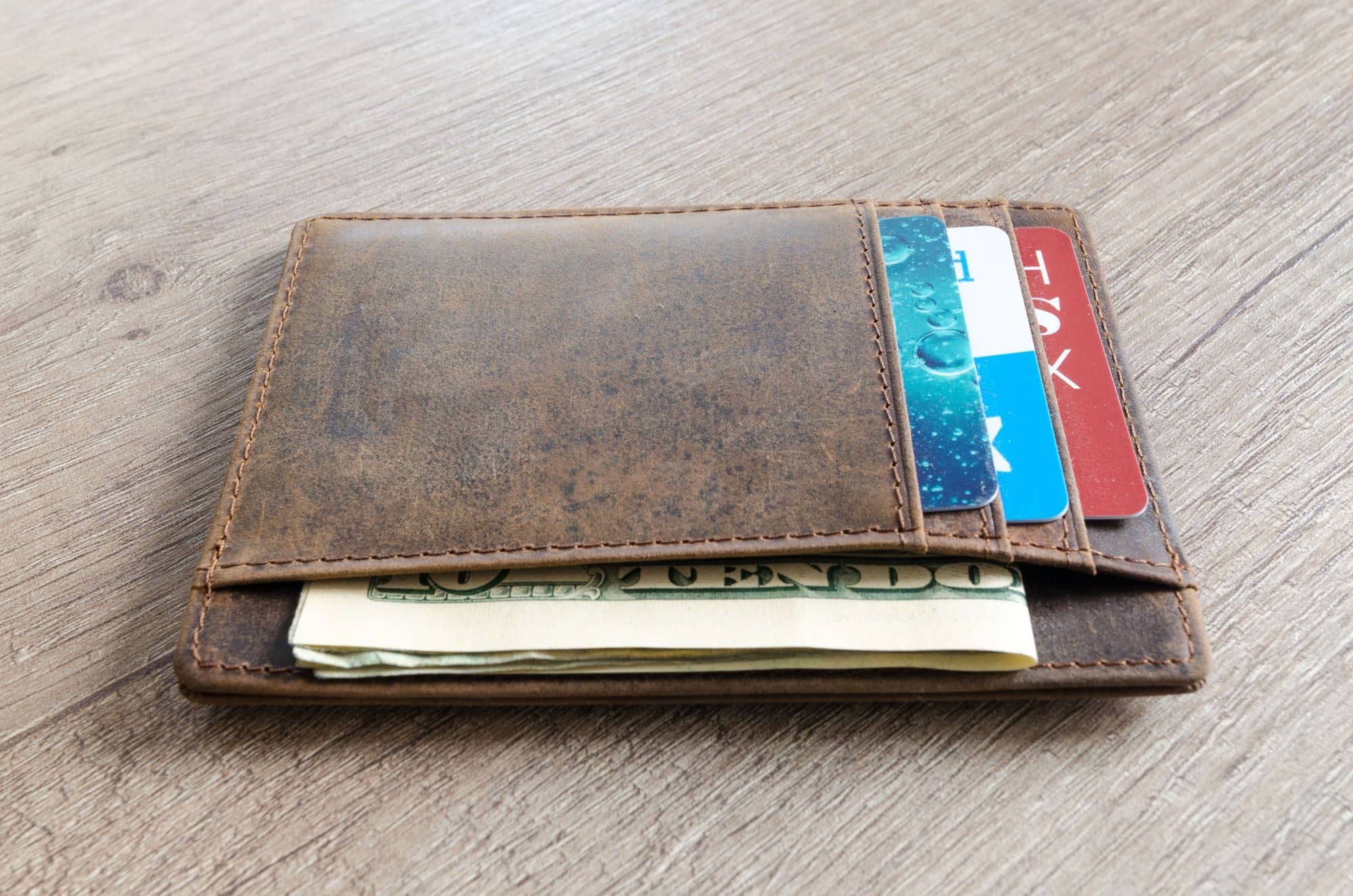 A brown leather wallet holding bank cards and folded cash