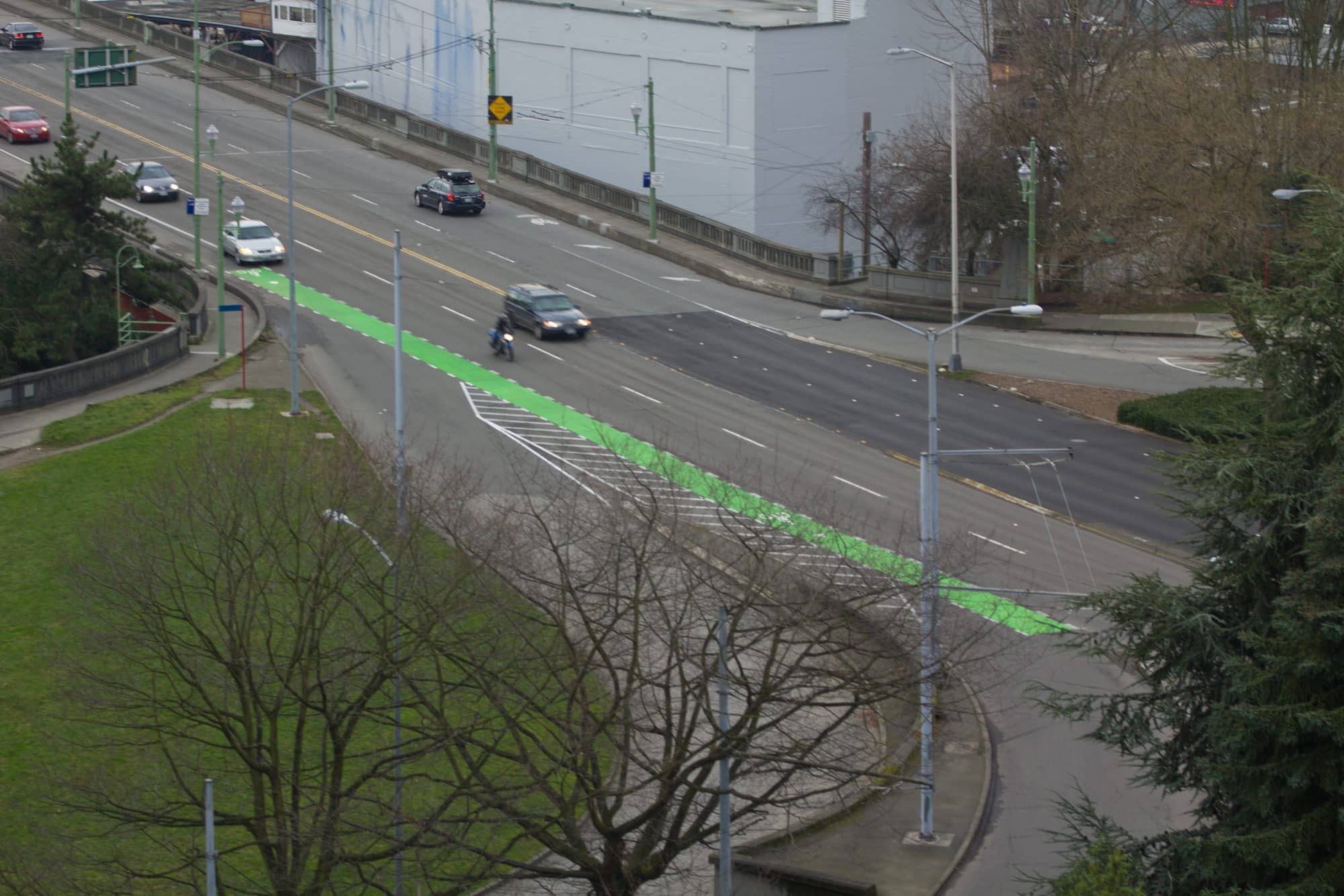 A bright green painted bike lane runs along a multi-lane city street, seen from above